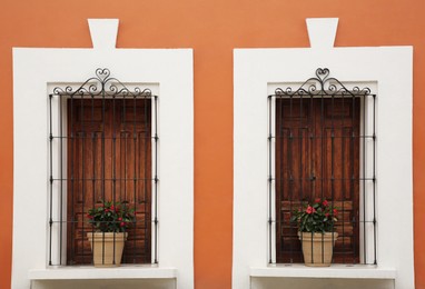 Photo of Orange building with wooden windows and potted plants on windowsills outdoors
