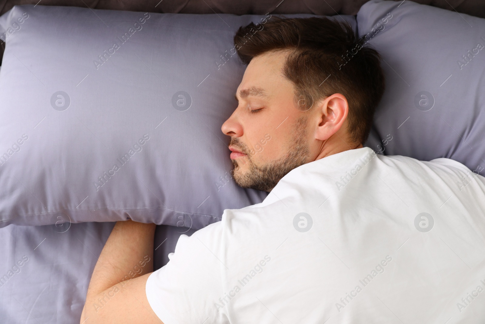 Photo of Handsome man sleeping on pillows, view from above. Bedtime