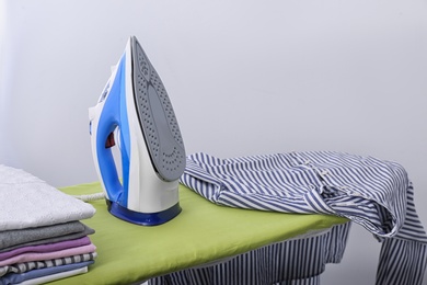 Photo of Modern electric iron and clothes on board indoors, space for text. Laundry day