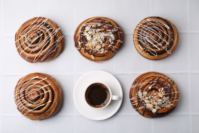 Photo of Delicious rolls with nuts, toppings and coffee cup on white tiled table, flat lay. Sweet buns