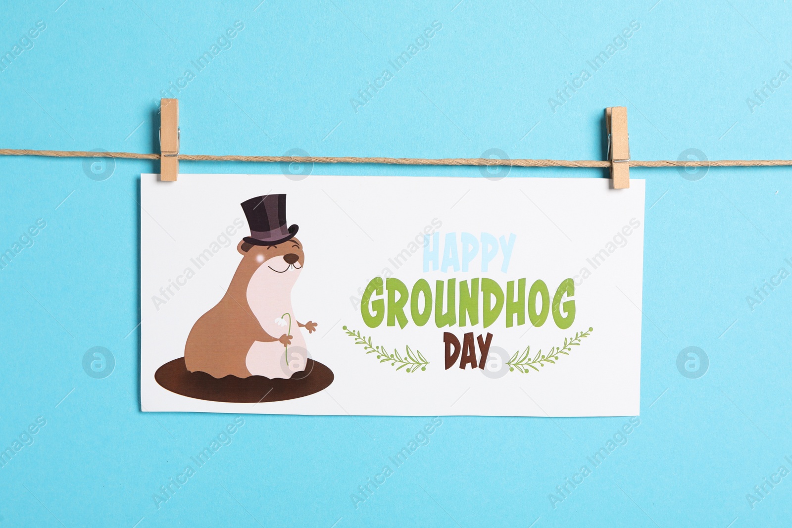 Photo of Happy Groundhog Day greeting card hanging on light blue background