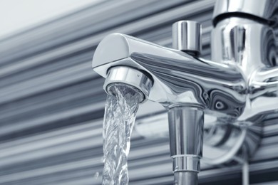 Photo of Water flowing from bath tap on blurred background, closeup