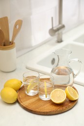 Photo of Jug, glasses with clear water and lemons on white table in kitchen