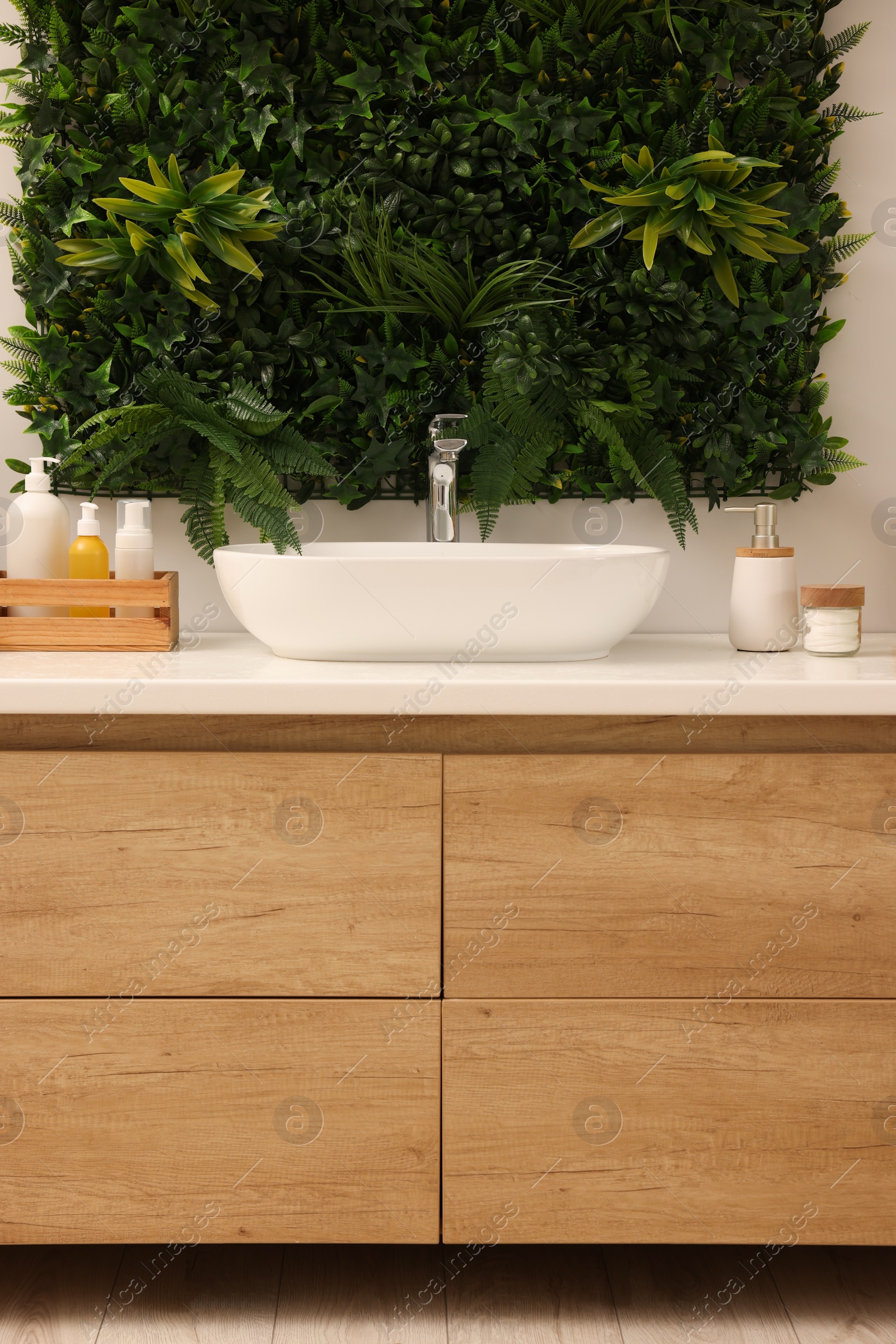 Photo of Green artificial plants, vanity and different personal care products in bathroom