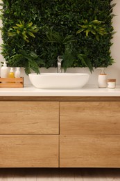 Green artificial plants, vanity and different personal care products in bathroom