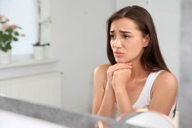 Young woman with eyelash loss problem looking in mirror indoors