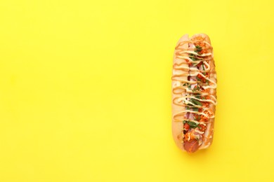 Photo of Delicious hot dog with bacon, carrot and parsley on yellow background, top view. Space for text