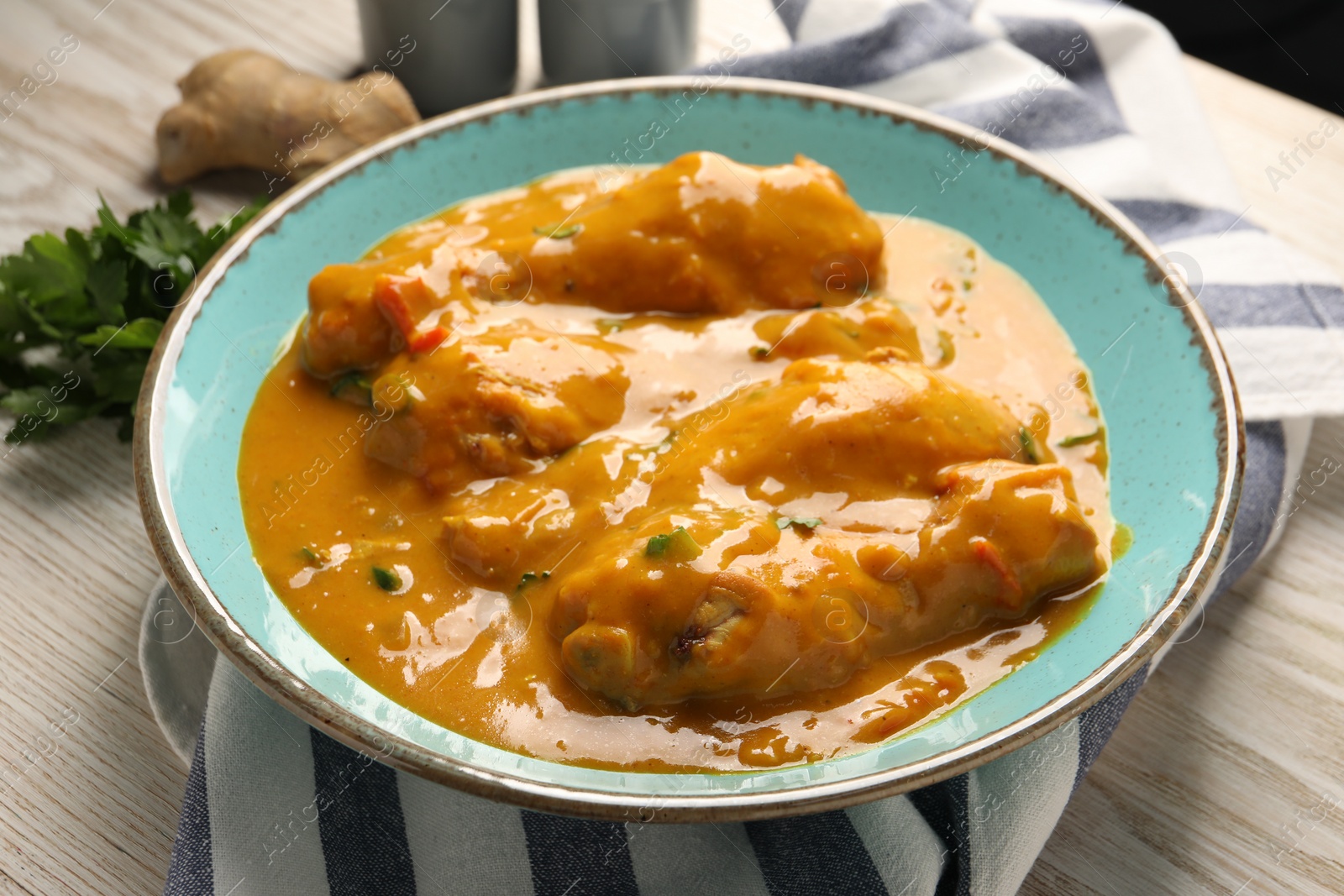 Photo of Tasty chicken curry, parsley and ginger on wooden table, closeup