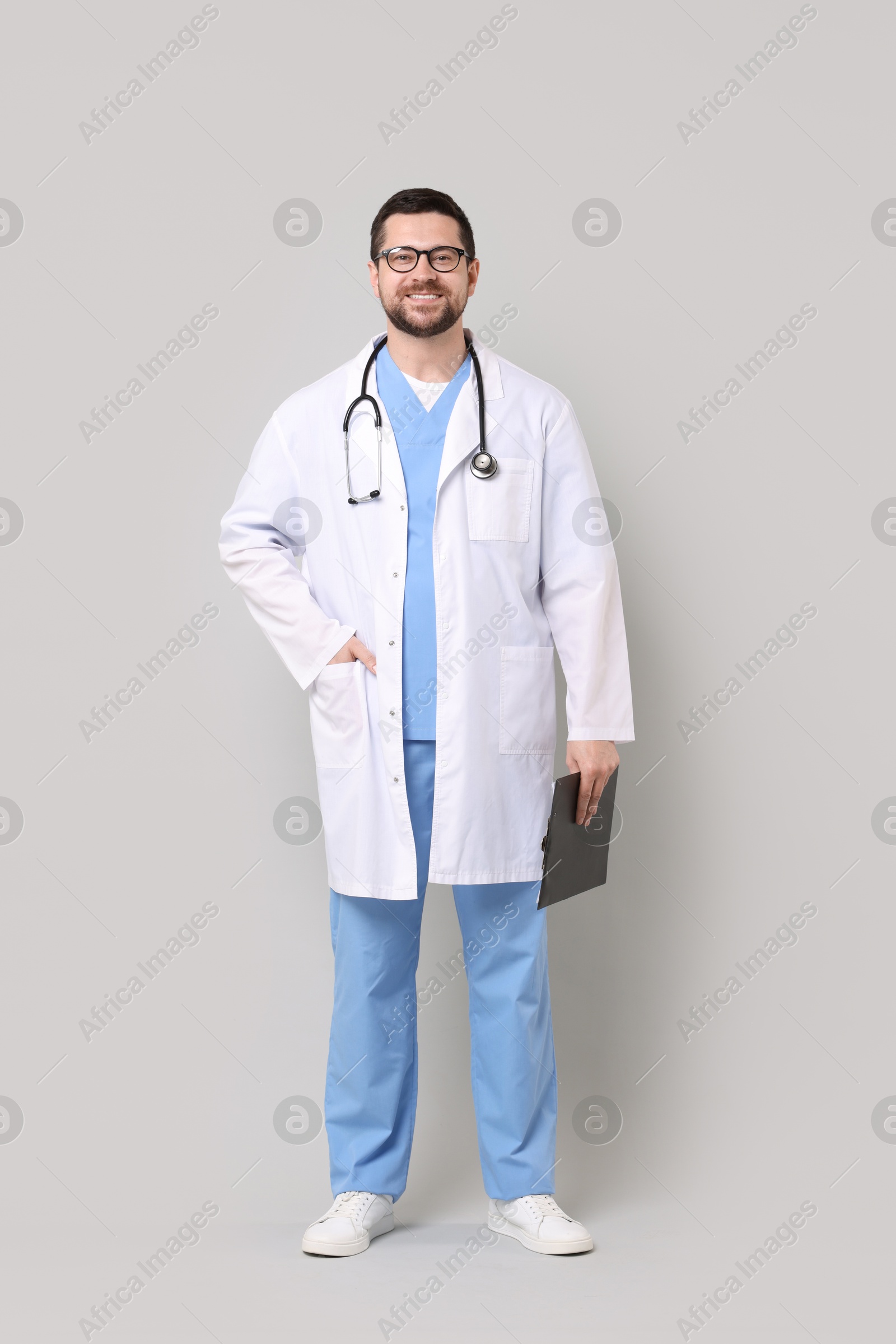 Photo of Smiling doctor with clipboard on light grey background