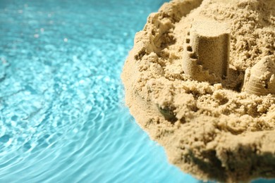 Photo of Pile of sand with beautiful castle on rippled water, closeup. Space for text
