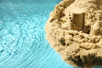 Pile of sand with beautiful castle on rippled water, closeup. Space for text