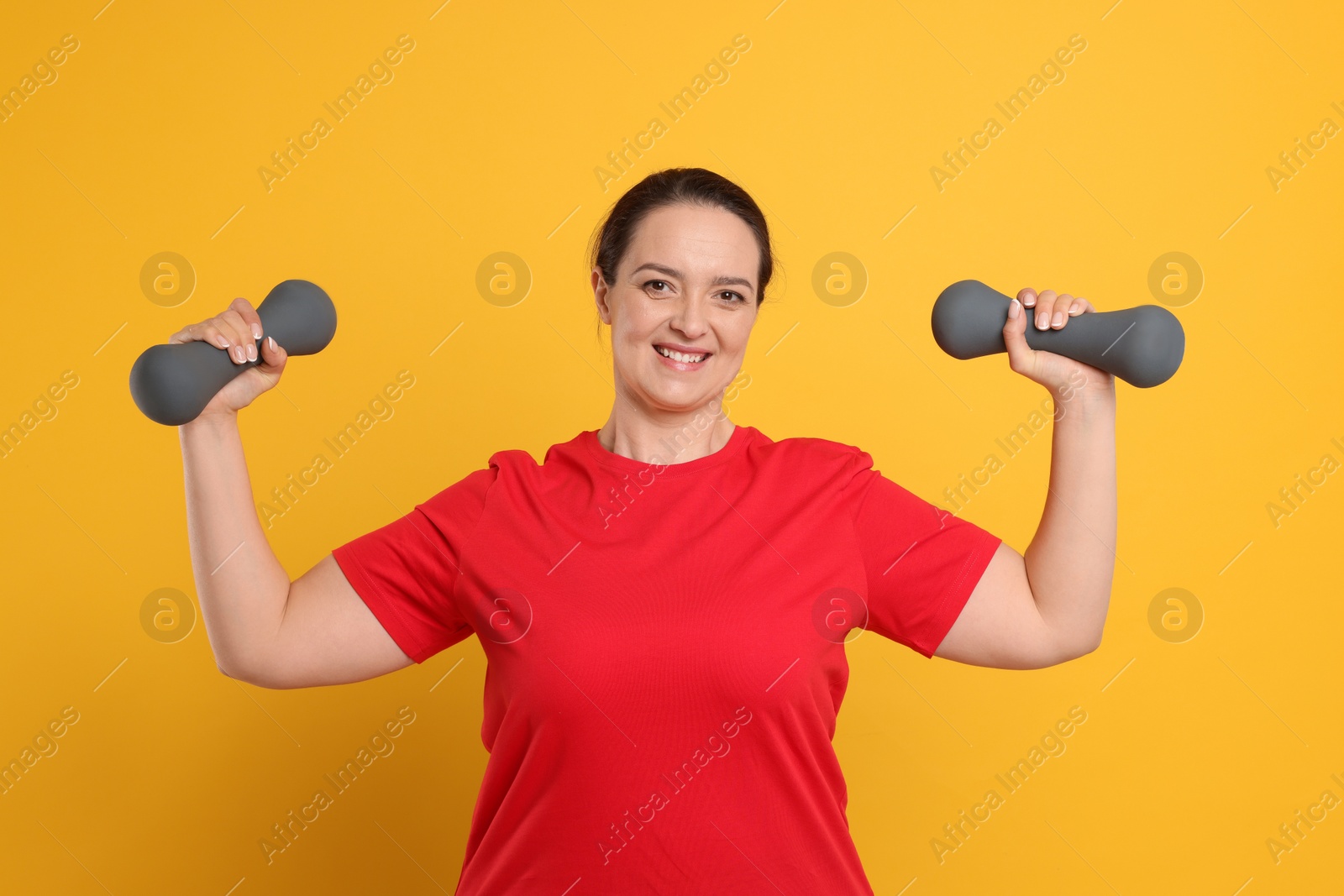 Photo of Happy overweight woman doing exercise with dumbbells on orange background