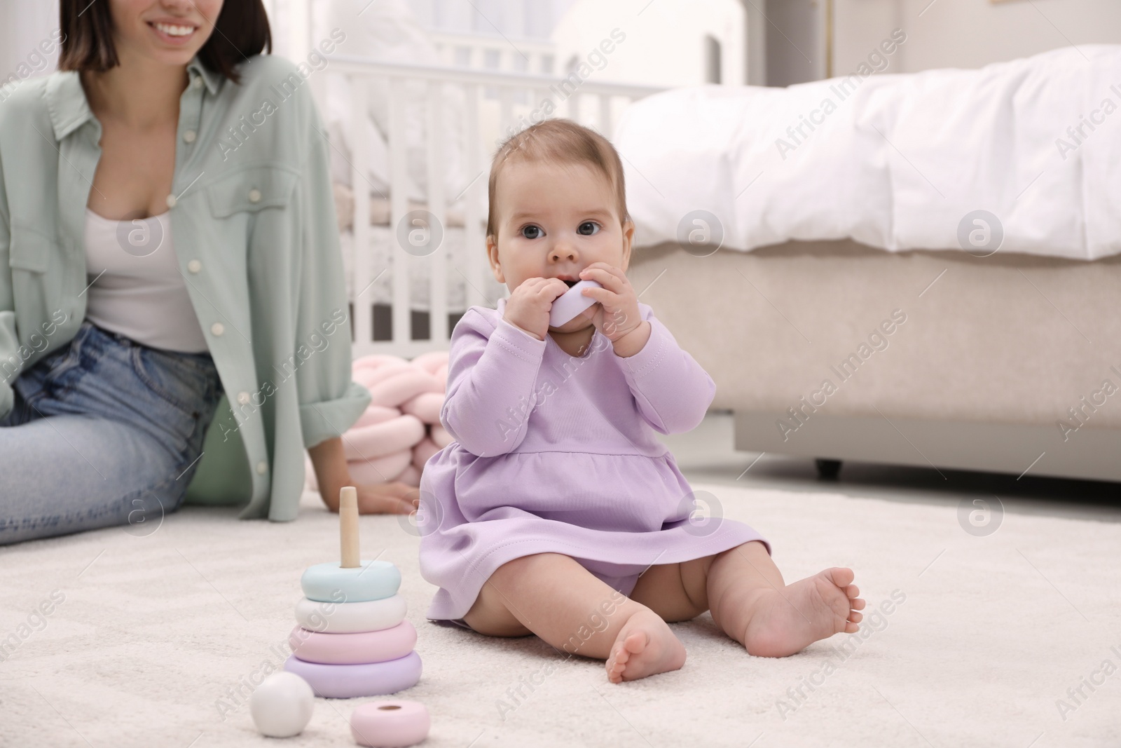 Photo of Cute baby girl playing with toy pyramid near mother on floor at home