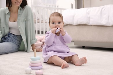 Photo of Cute baby girl playing with toy pyramid near mother on floor at home