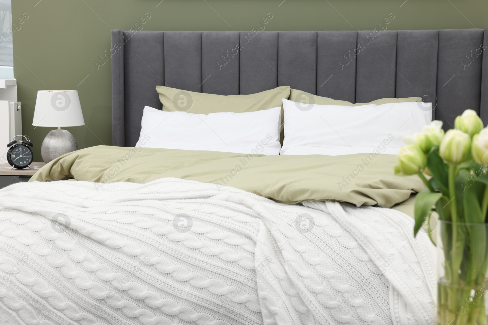 Photo of Comfortable bed, lamp on bedside table and vase of tulips in bedroom. Interior design