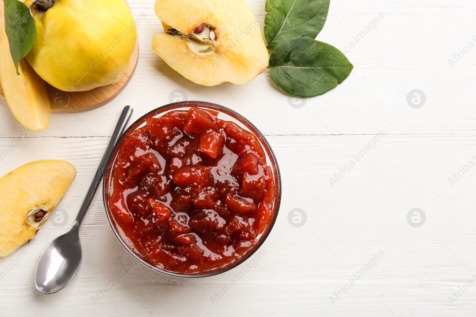 Photo of Delicious quince jam, fruits, leaves and spoon on white wooden table, flat lay. Space for text