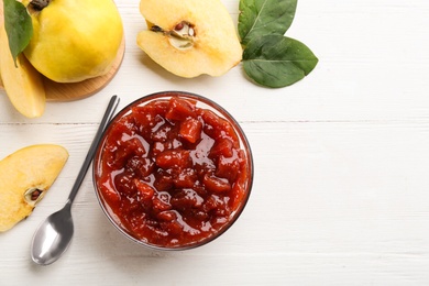 Photo of Delicious quince jam, fruits, leaves and spoon on white wooden table, flat lay. Space for text