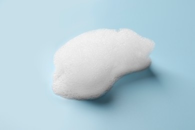 Photo of Drop of fluffy soap foam on light blue background