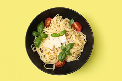 Photo of Bowl of delicious pasta with brie cheese, tomatoes and basil leaves on yellow background, top view