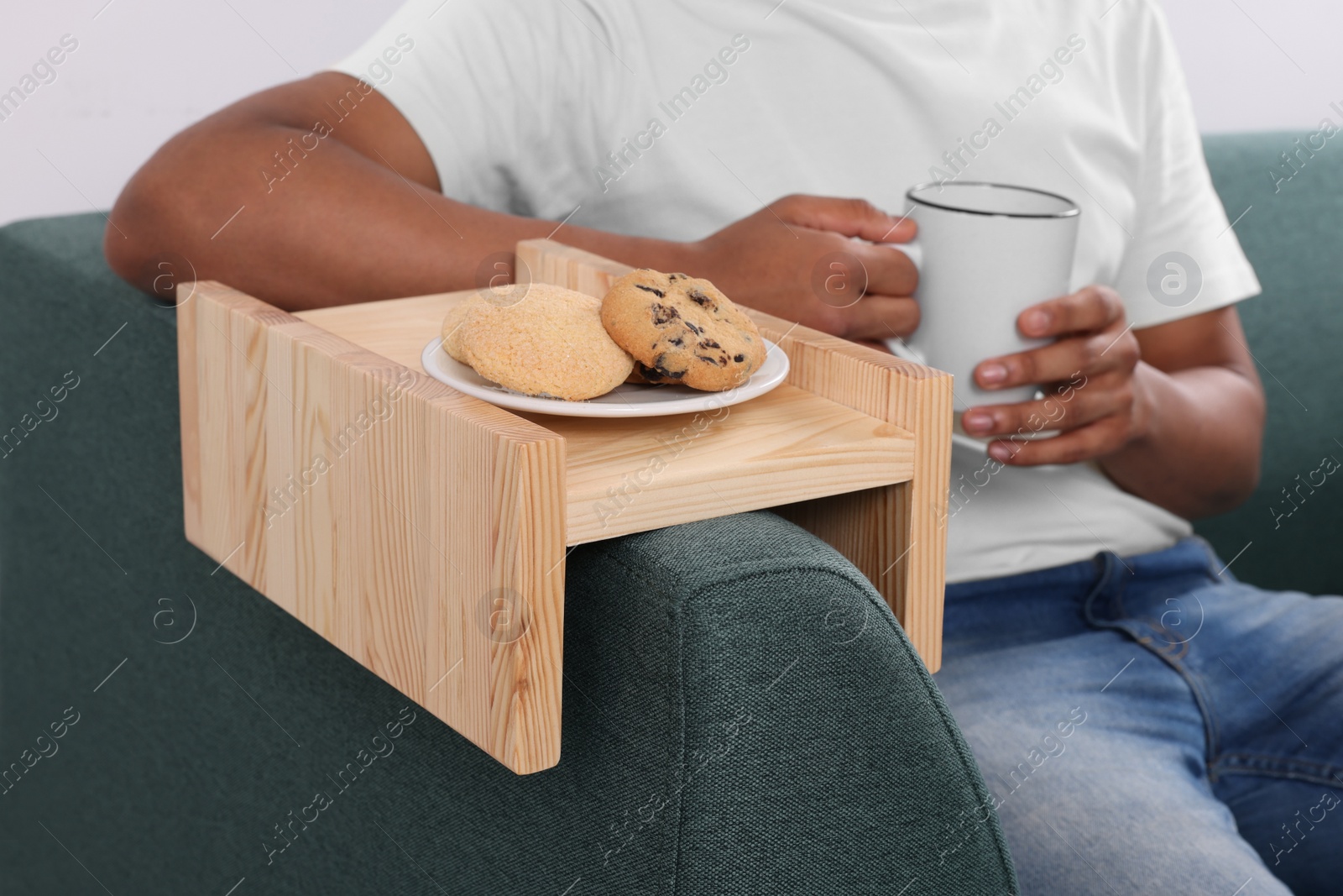 Photo of Cookies on sofa armrest wooden table. Man holding cup of drink at home, closeup