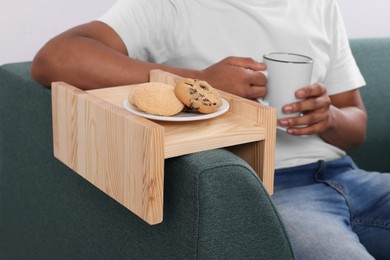 Photo of Cookies on sofa armrest wooden table. Man holding cup of drink at home, closeup