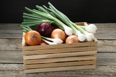 Crate with different kinds of onions on wooden table