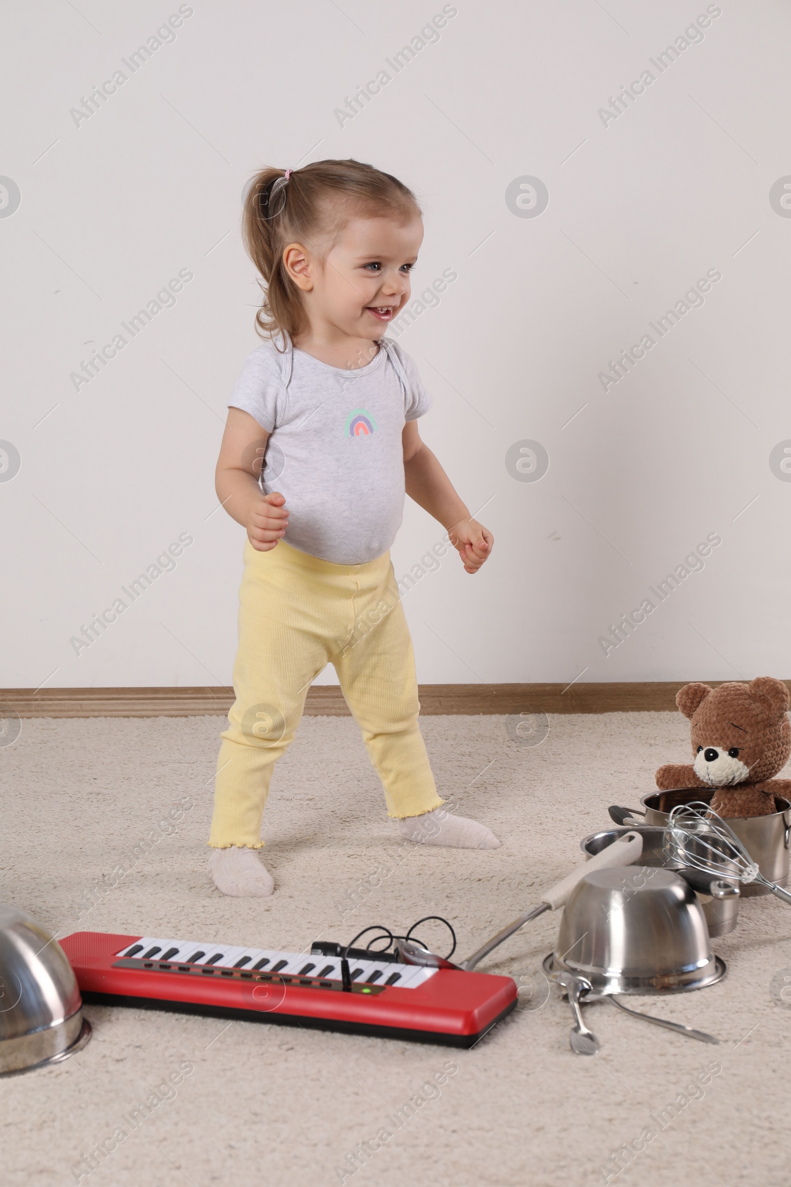 Photo of Cute little girl with cookware and toy piano at home