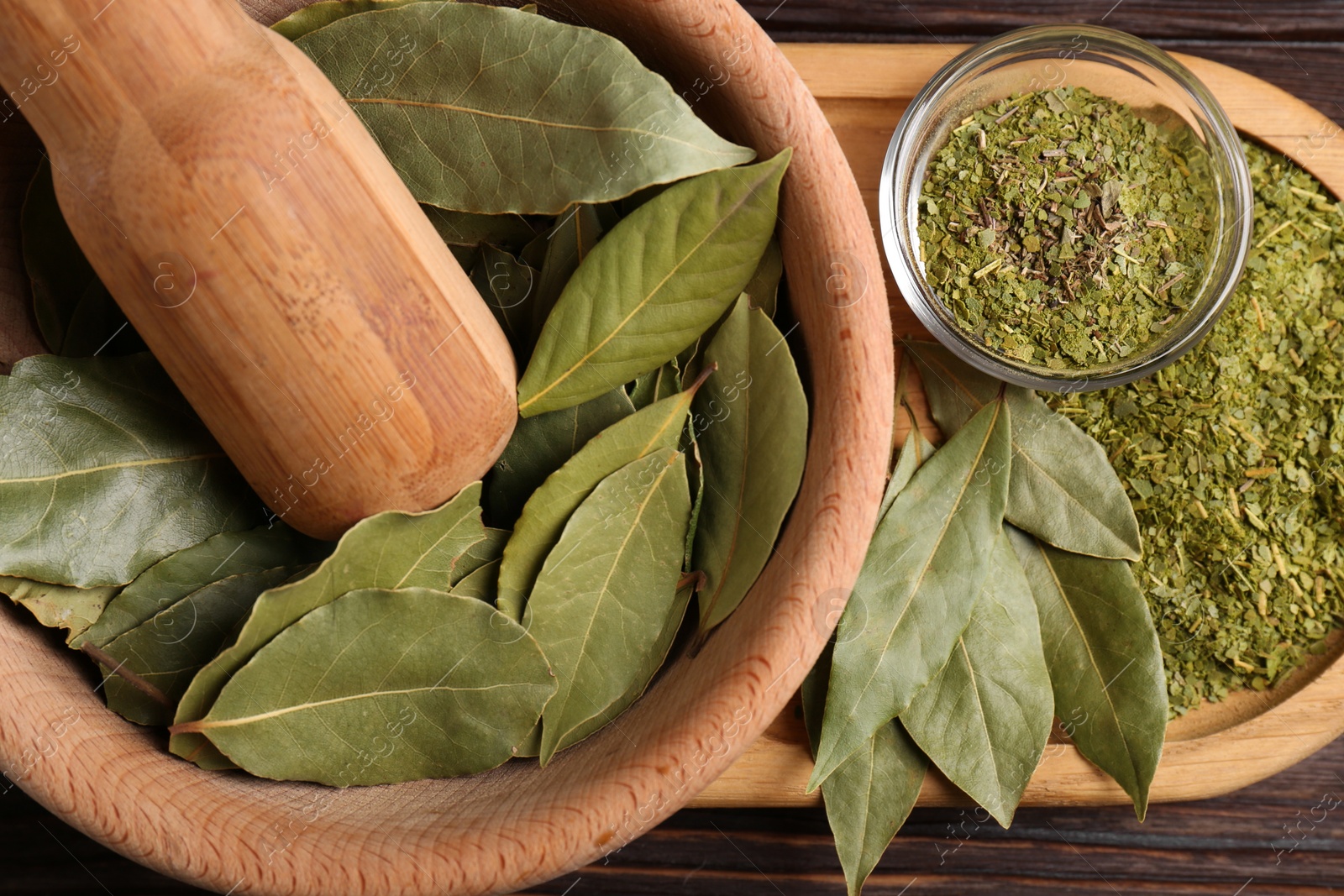Photo of Bay leaves in mortar with pestle on wooden table, closeup