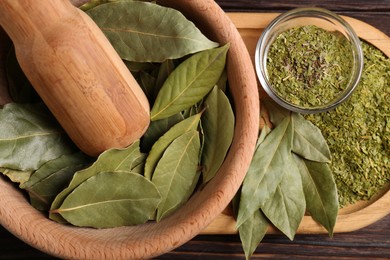 Photo of Bay leaves in mortar with pestle on wooden table, closeup