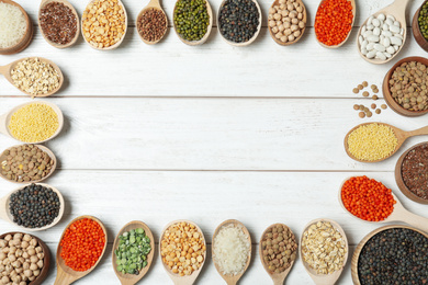 Photo of Frame made with different grains and cereals on white wooden table, top view. Space for text