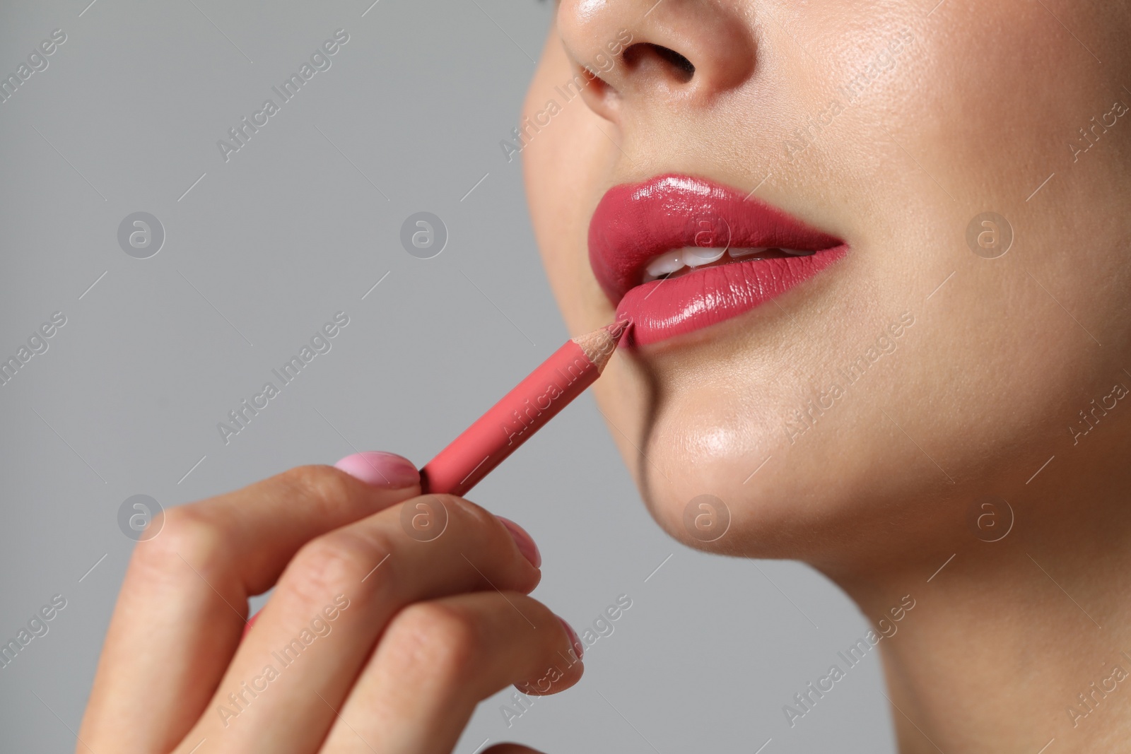 Photo of Young woman applying beautiful pink lip pencil on grey background, closeup