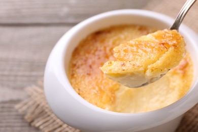 Taking delicious creme brulee with spoon from bowl at table, closeup