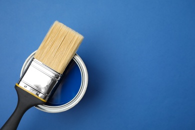 Photo of Open can with paint and brush on blue background, top view. Space for text