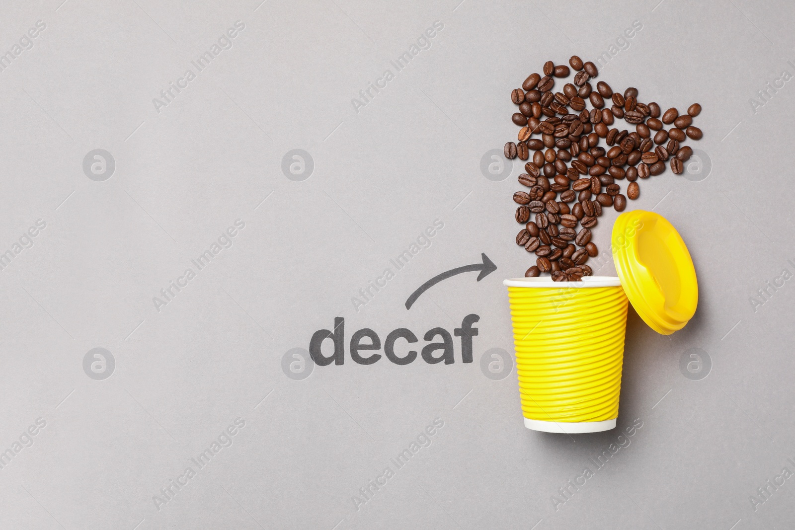 Photo of Word Decaf and arrow pointing at takeaway paper cup with coffee beans on light grey background, flat lay. Space for text