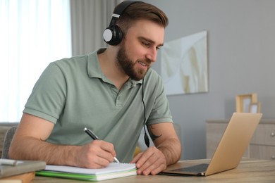 Young man taking notes during online webinar at table indoors