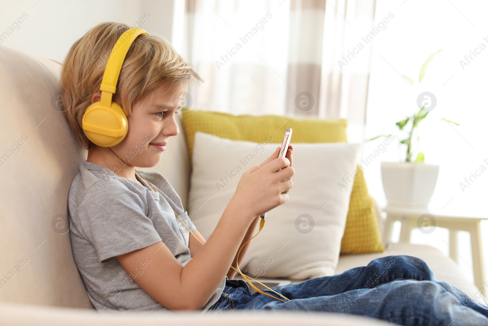 Photo of Cute little boy with headphones and smartphone listening to audiobook at home