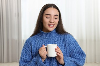 Photo of Happy young woman holding white ceramic mug at home