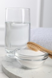 Bamboo toothbrush, bowl of baking soda and glass of water on white table, closeup