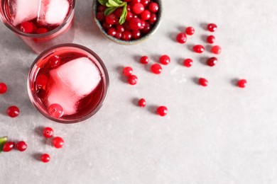 Photo of Tasty cranberry juice with ice cubes in glasses and fresh berries on light grey table, flat lay. Space for text