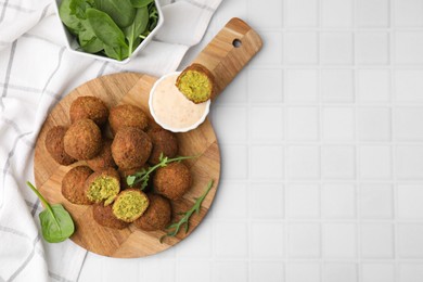 Photo of Delicious falafel balls, herbs and sauce on white tiled table, top view. Space for text