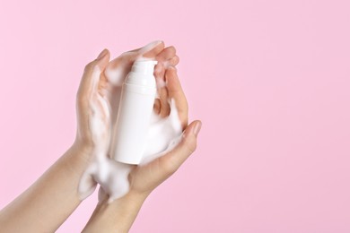 Photo of Woman with bottle of care product and cleansing foam on pink background, closeup. Space for text