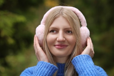 Photo of Young beautiful woman wearing warm earmuffs outdoors