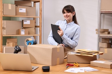 Photo of Parcel packing. Post office worker with clipboard at wooden table indoors