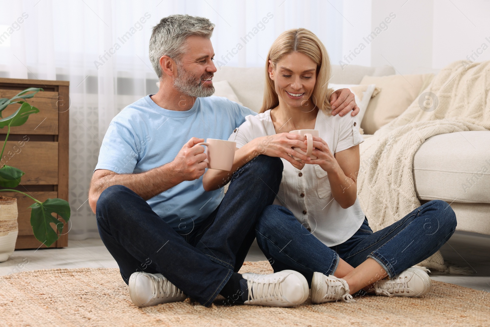 Photo of Happy affectionate couple with cups of hot drinks on floor at home. Romantic date