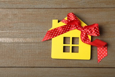 Yellow house model with bow on wooden table, top view and space for text. Housewarming party