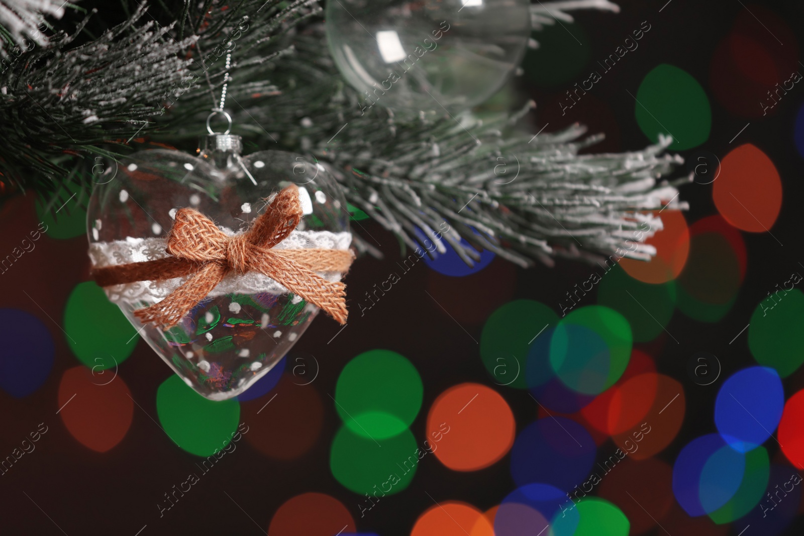 Photo of Heart shaped holiday bauble hanging on Christmas tree against blurred festive lights, closeup. Space for text