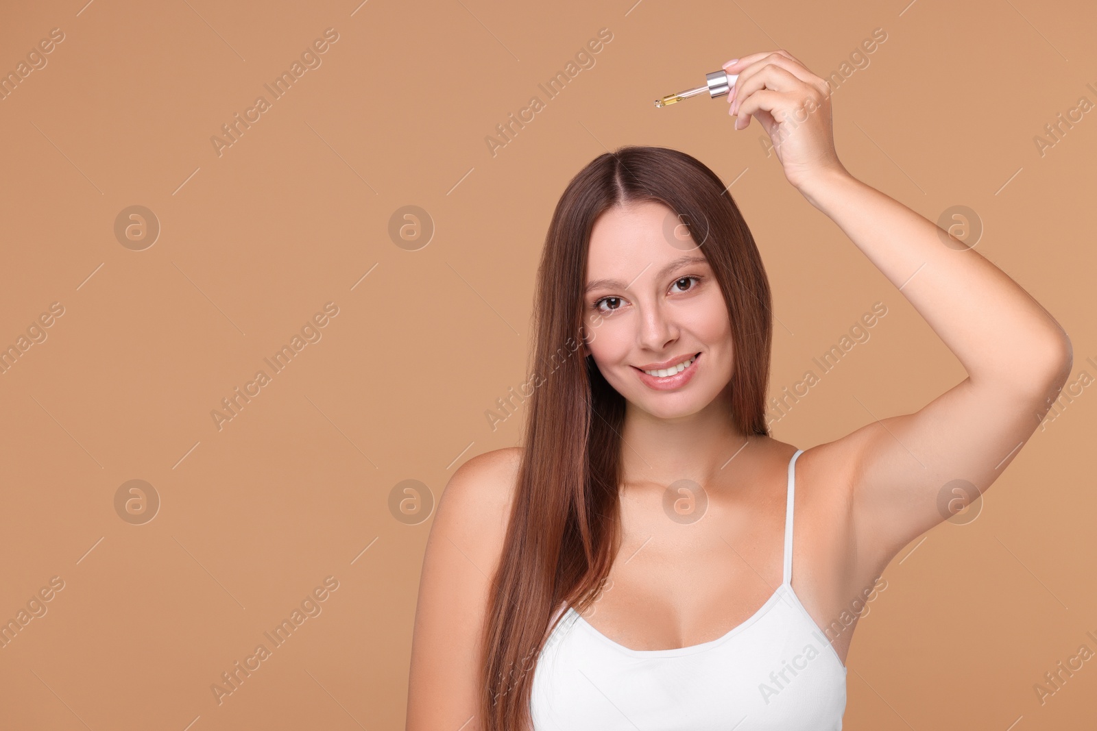 Photo of Beautiful woman applying serum onto hair on beige background, space for text