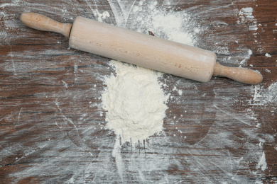 Photo of Flour and rolling pin on wooden table, top view