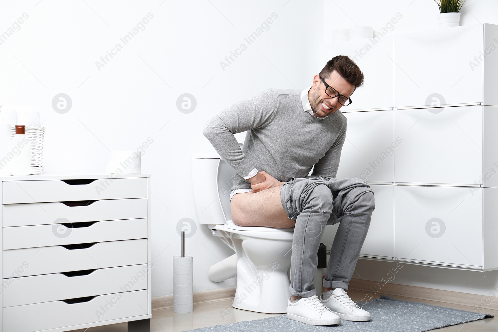 Photo of Man with stomach ache sitting on toilet bowl in bathroom