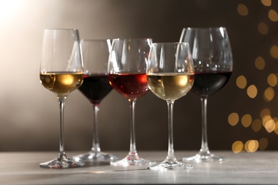 Photo of Glasses with different wines on grey table against defocused lights